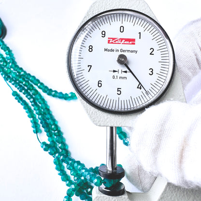 A dial gauge measures the green onyx faceted rondelle gemstone.