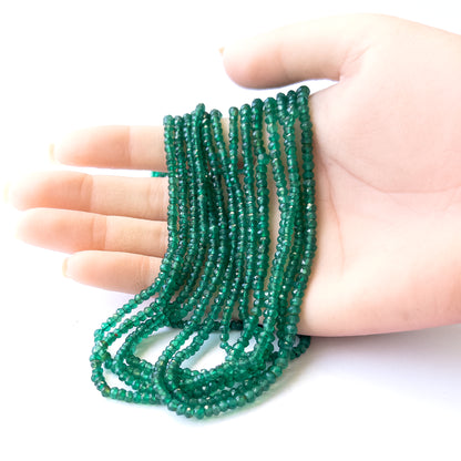 A person holds delicate strands of Green Onyx beads, showcasing their faceted rondelle design.