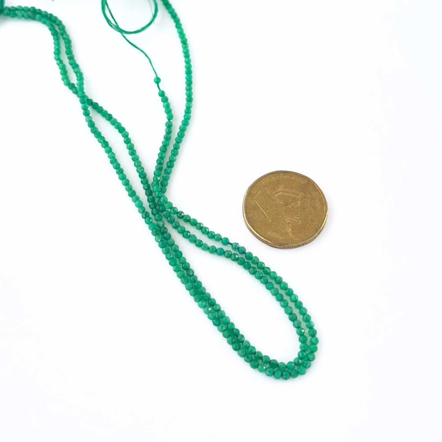 A coin is placed near delicate strands of Green Onyx beads for scale