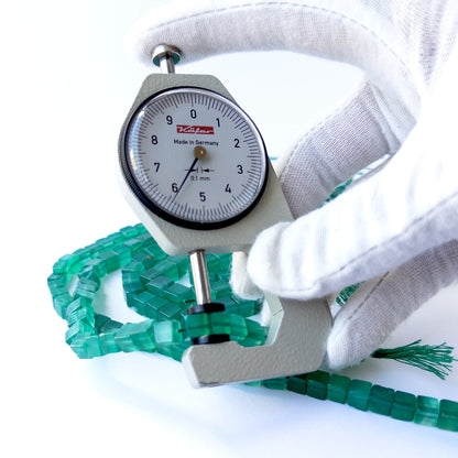 A dial gauge measures the Green Onyx smooth cube 5.5–7mm gemstone.