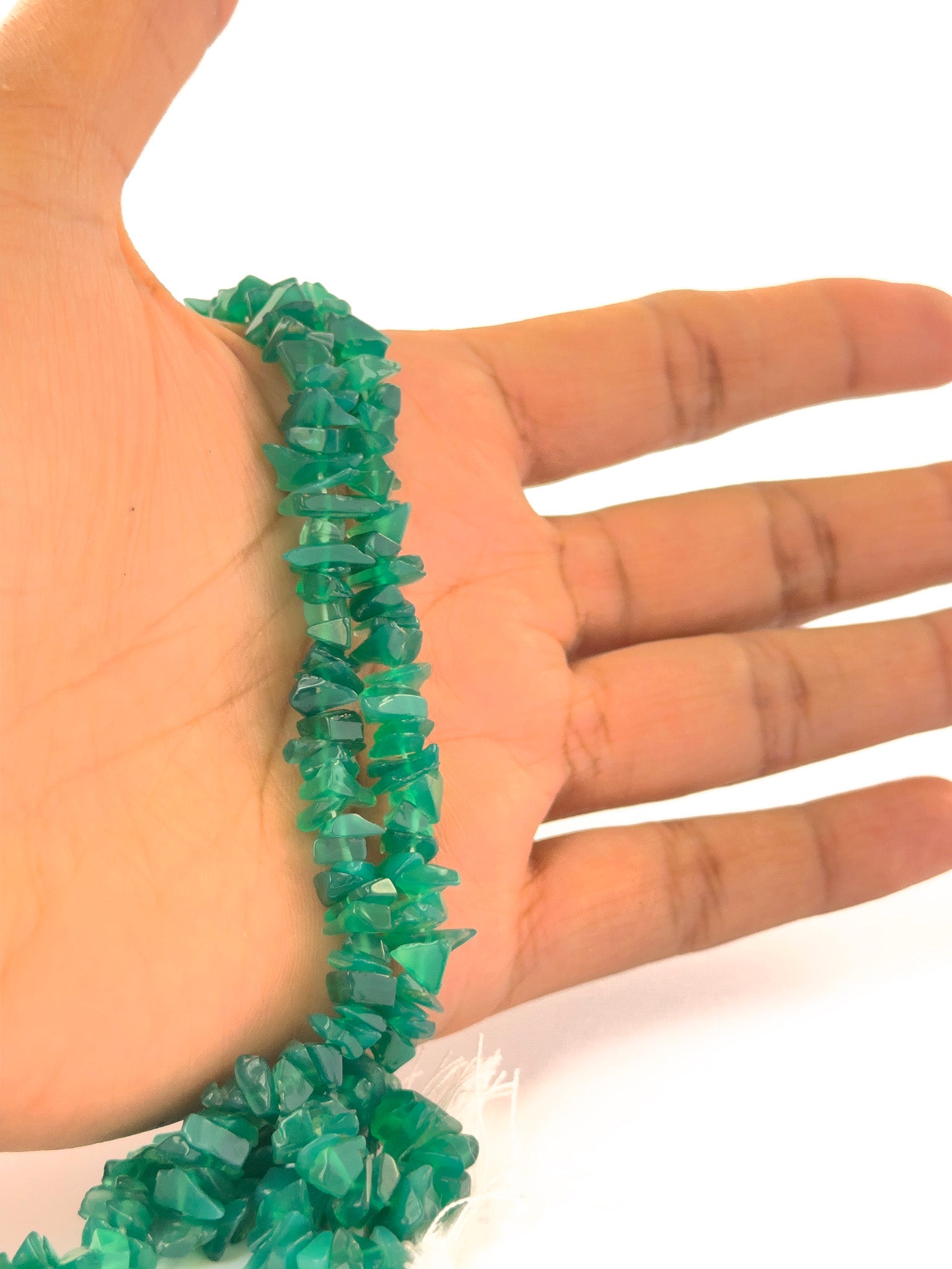 A person holding raw Green Onyx gemstone chips, irregular 5–10mm beads arranged on a 46cm strand.