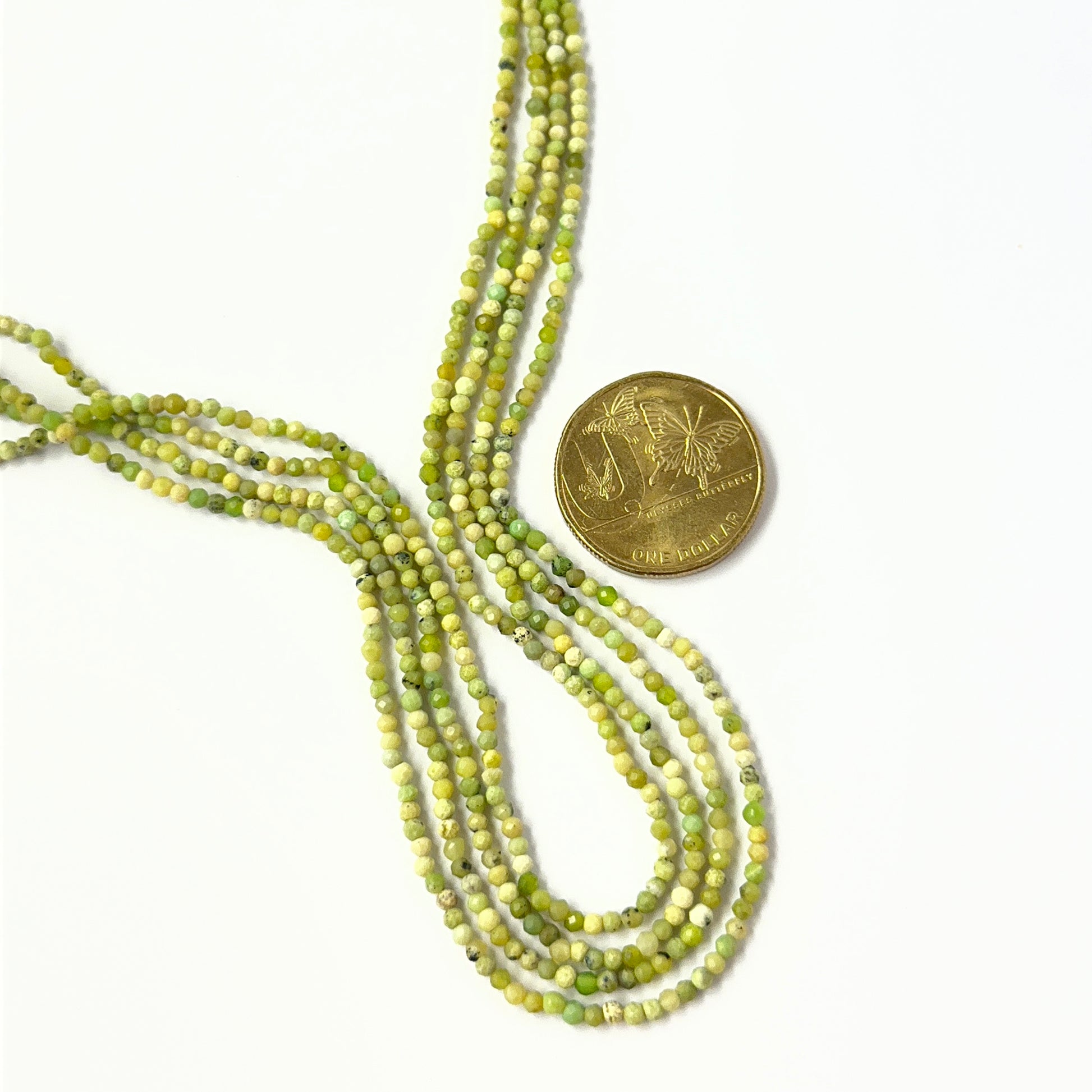 A coin is placed near delicate strands of Green Opal beads for scale.