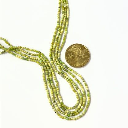A coin is placed near delicate strands of Green Opal beads for scale.