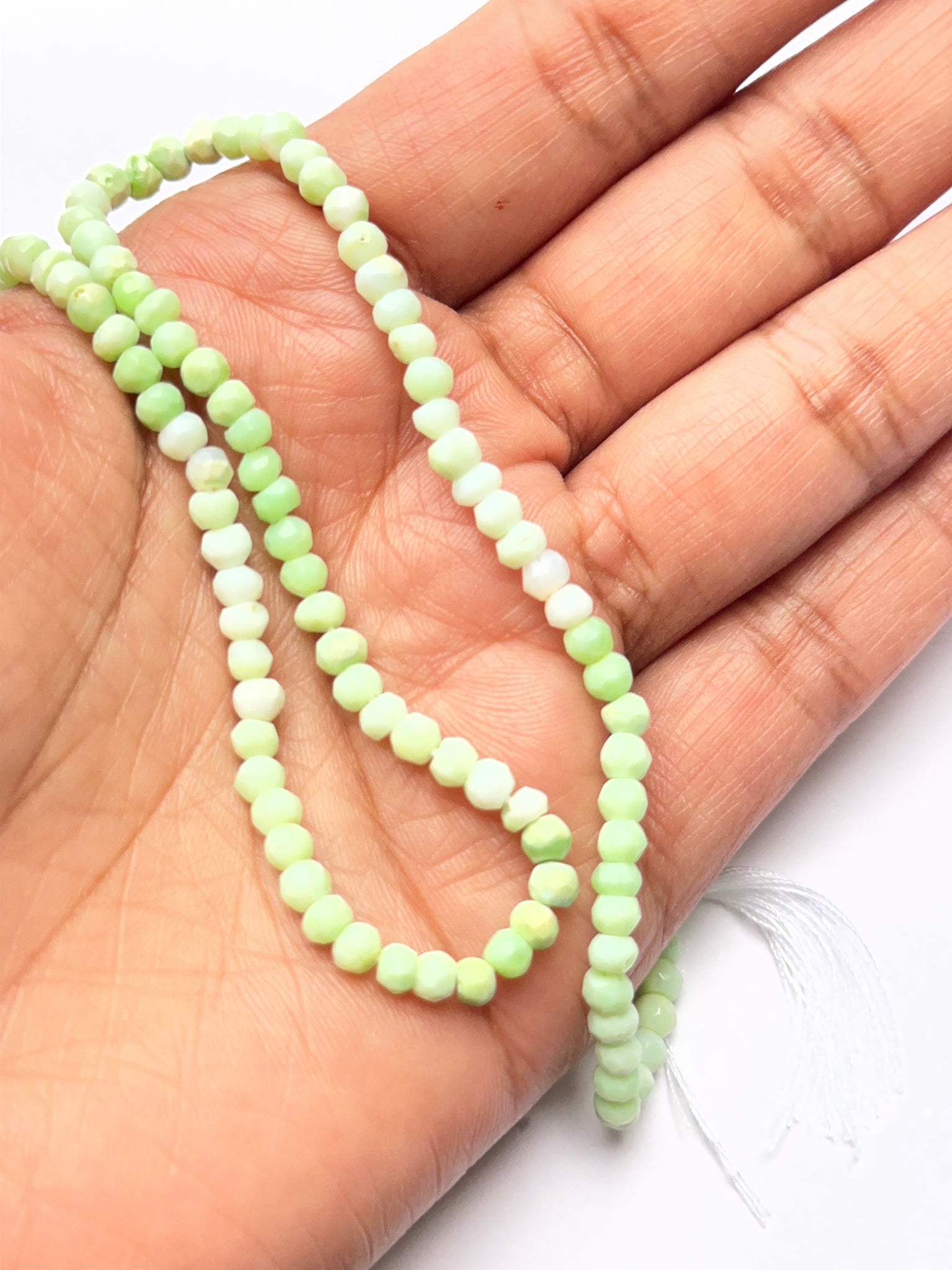 A person holds delicate strands of Emerald beads, showcasing their smooth design.