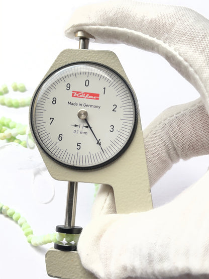 A dial gauge measures the Emerald undrilled rough 25–28mm gemstone.