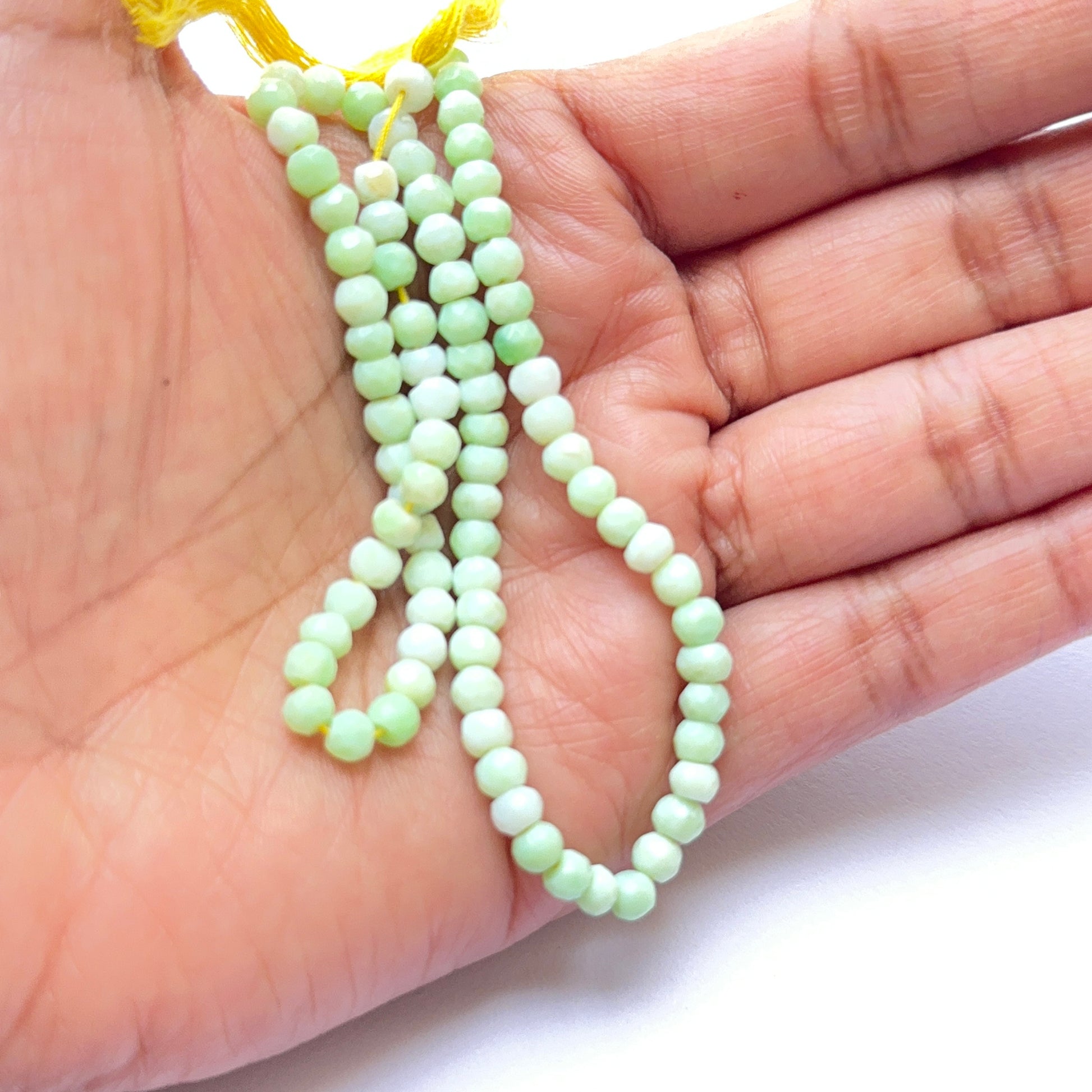 A person holds delicate strands of Green Opal beads, showcasing their smooth design.