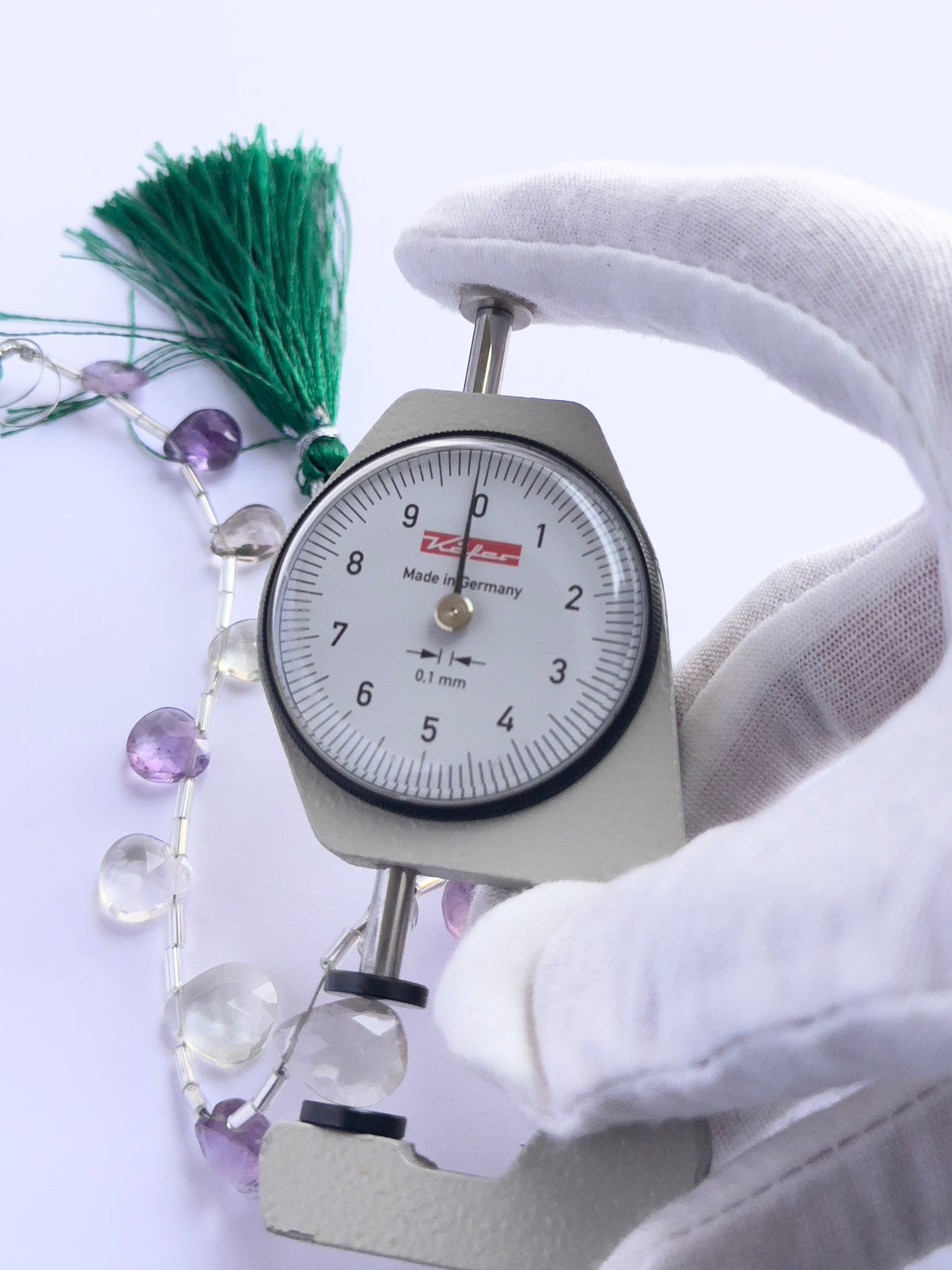 A dial gauge measures the Green and Purple Amethyst faceted briolette 7–10mm gemstone.