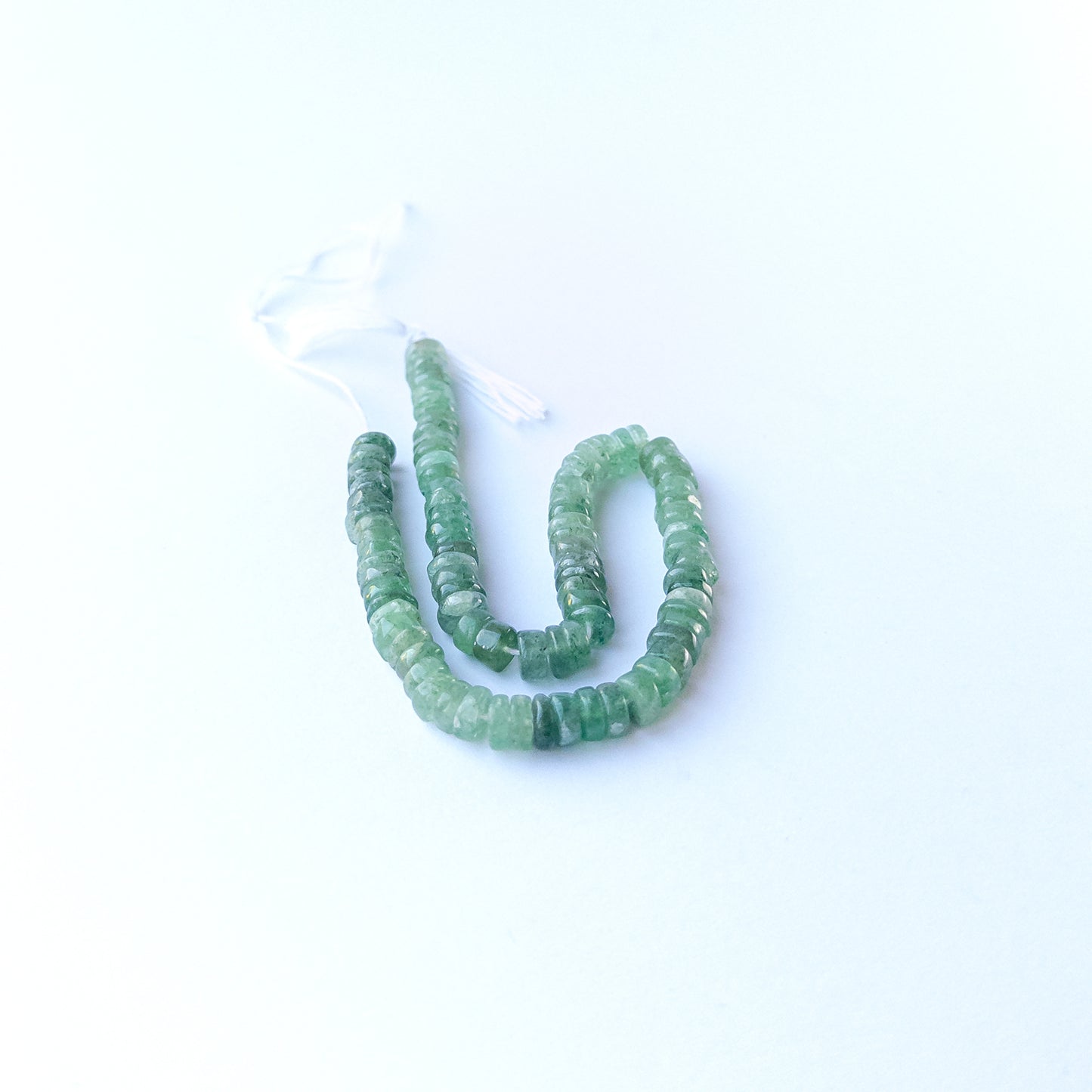 Green Strawberry Quartz smooth wheel gemstone beads arranged in a soft green strand for DIY jewellery.