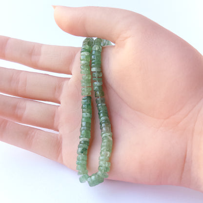 A person holds delicate strands of Green Strawberry Quartz beads, showcasing their smooth wheels design.