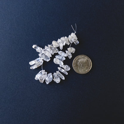 A coin is placed near delicate pieces of Herkimer Diamond drilled rough beads for scale.