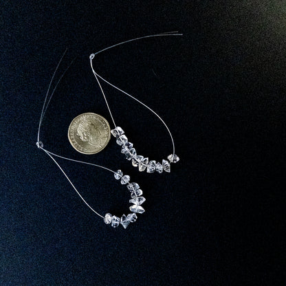 A coin is placed near delicate pieces of Herkimer Diamond drilled rough beads for scale.