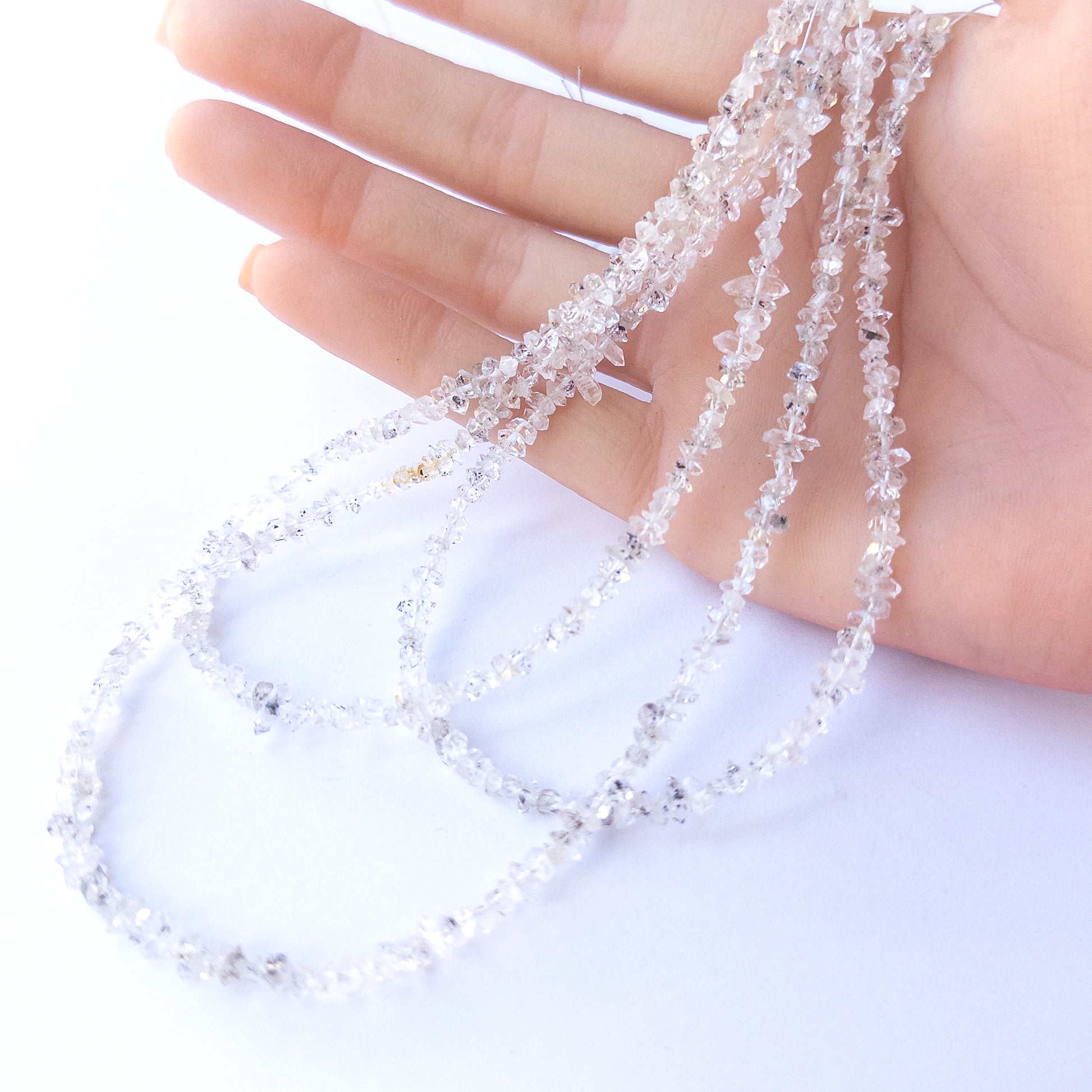 A person holds delicate strands of Herkimer Diamond beads, showcasing their chip‑cut design.