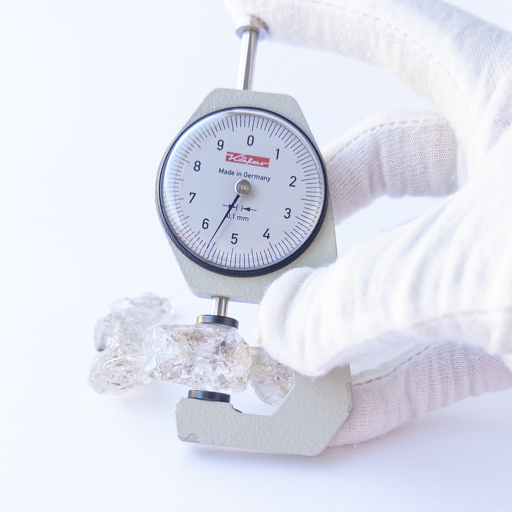 A dial gauge measures the Herkimer Diamond drilled rough 15.5–17mm gemstone.