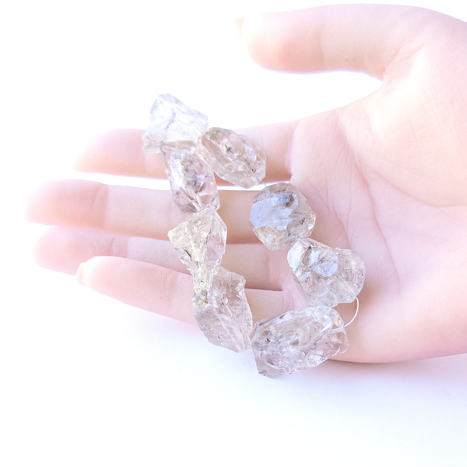 A person holds delicate strands of Herkimer Diamond beads, showcasing their drilled rough design.