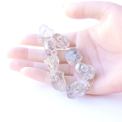 A person holds delicate strands of Herkimer Diamond beads, showcasing their drilled rough design.