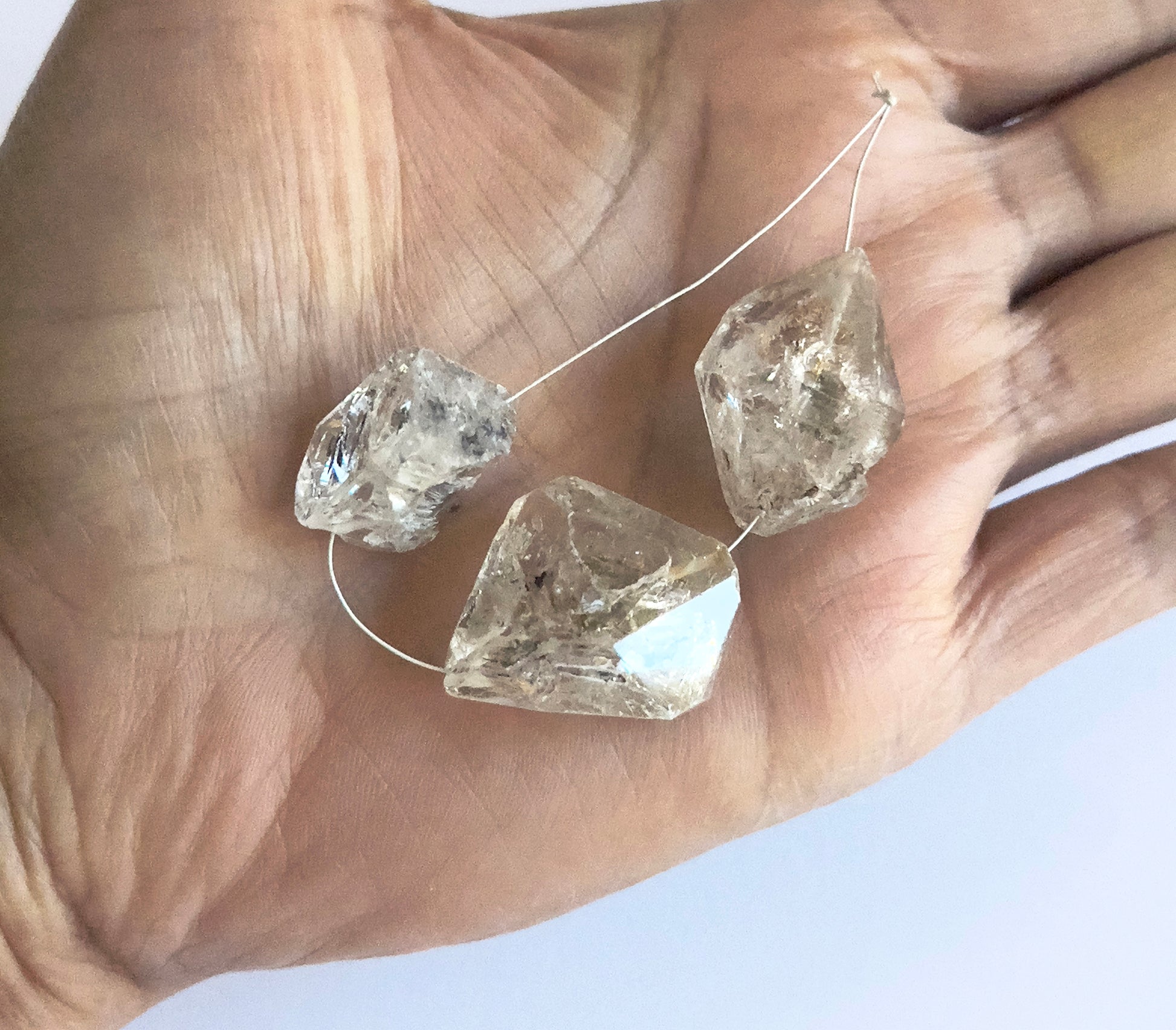 A person holds delicate strands of Herkimer Diamond beads, showcasing their raw brillance.