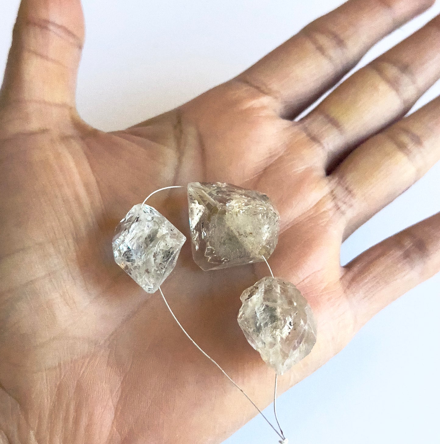 A person holds delicate strands of Herkimer Diamond beads, showcasing their natural and raw design.