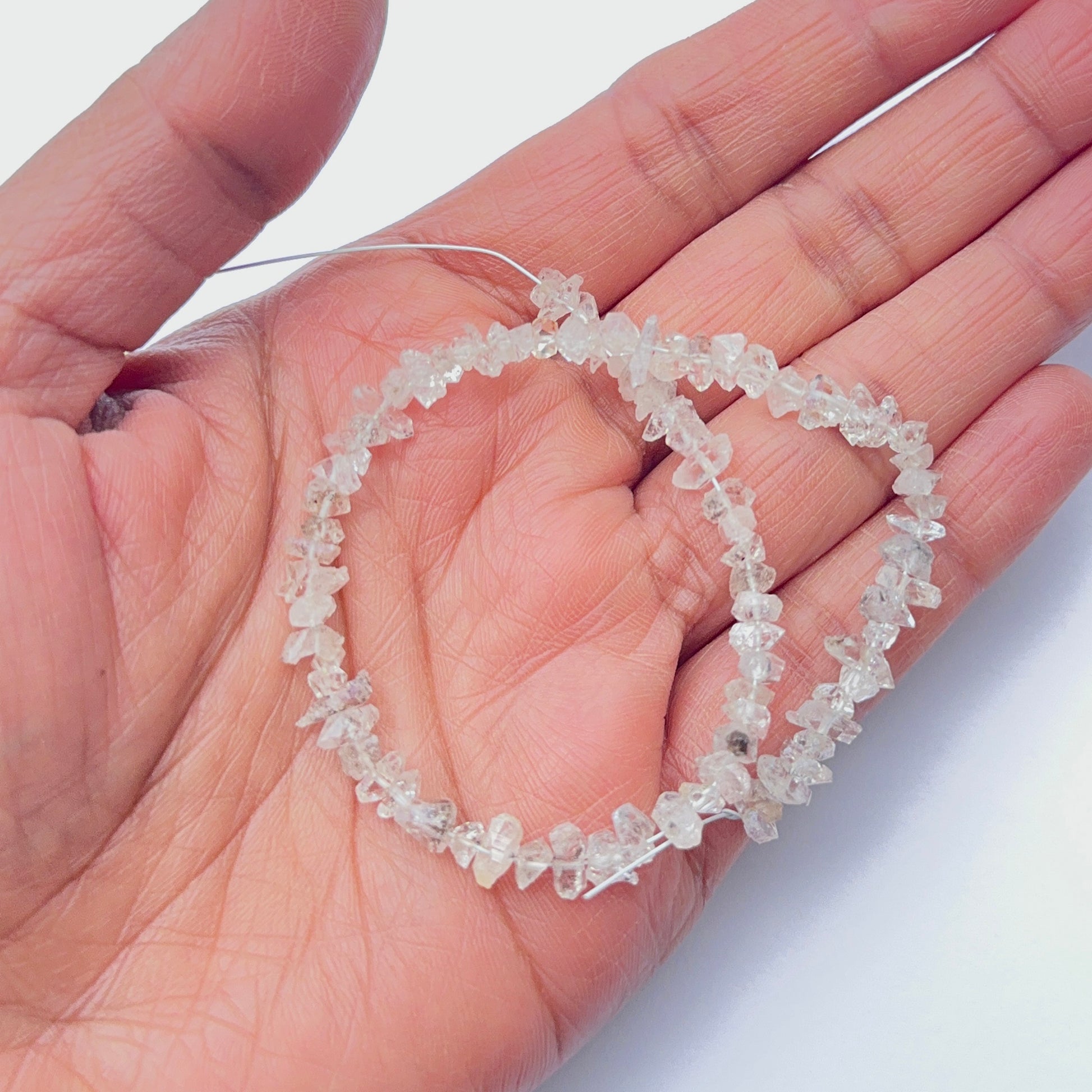 A person holds delicate strands of Herkimer Diamond rough beads, showcasing their smooth design.
