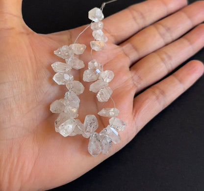 A person holds delicate strands of Herkimer Diamond beads, showcasing their smooth design.