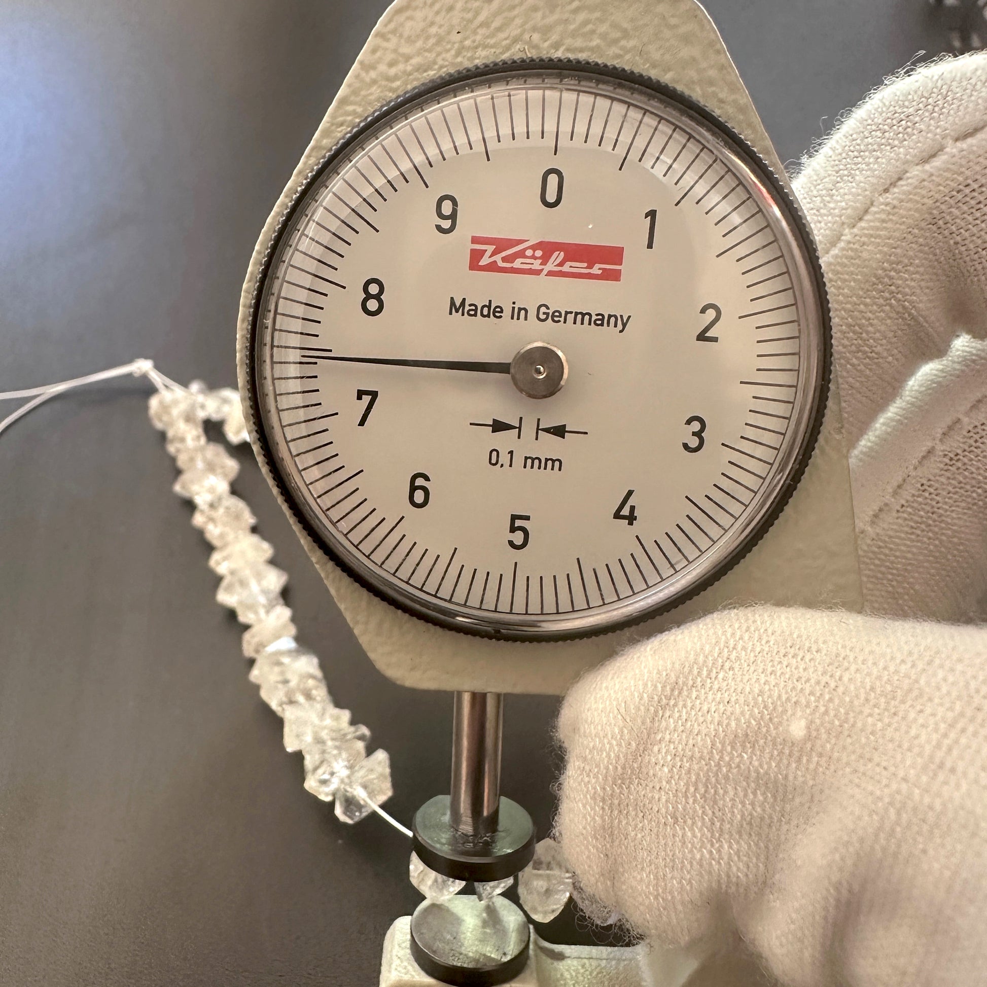 A dial gauge measures the Herkimer Diamond rough cut 4.5-5mm gemstone.