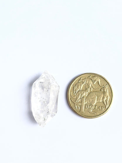 Herkimer Diamond rough photographed to show its unpolished finish and genuine brilliance and next to a coin for scale.