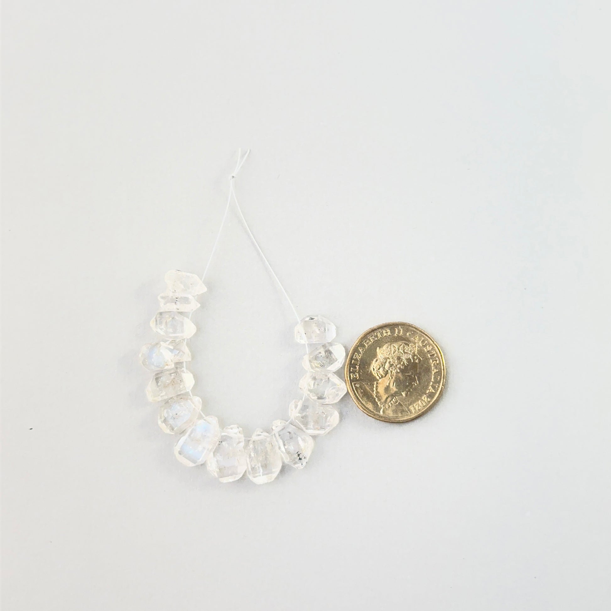 Large rough Herkimer Diamond stones on a strand for artisan fashion and bespoke jewellery gifts place next to a coin for scale.