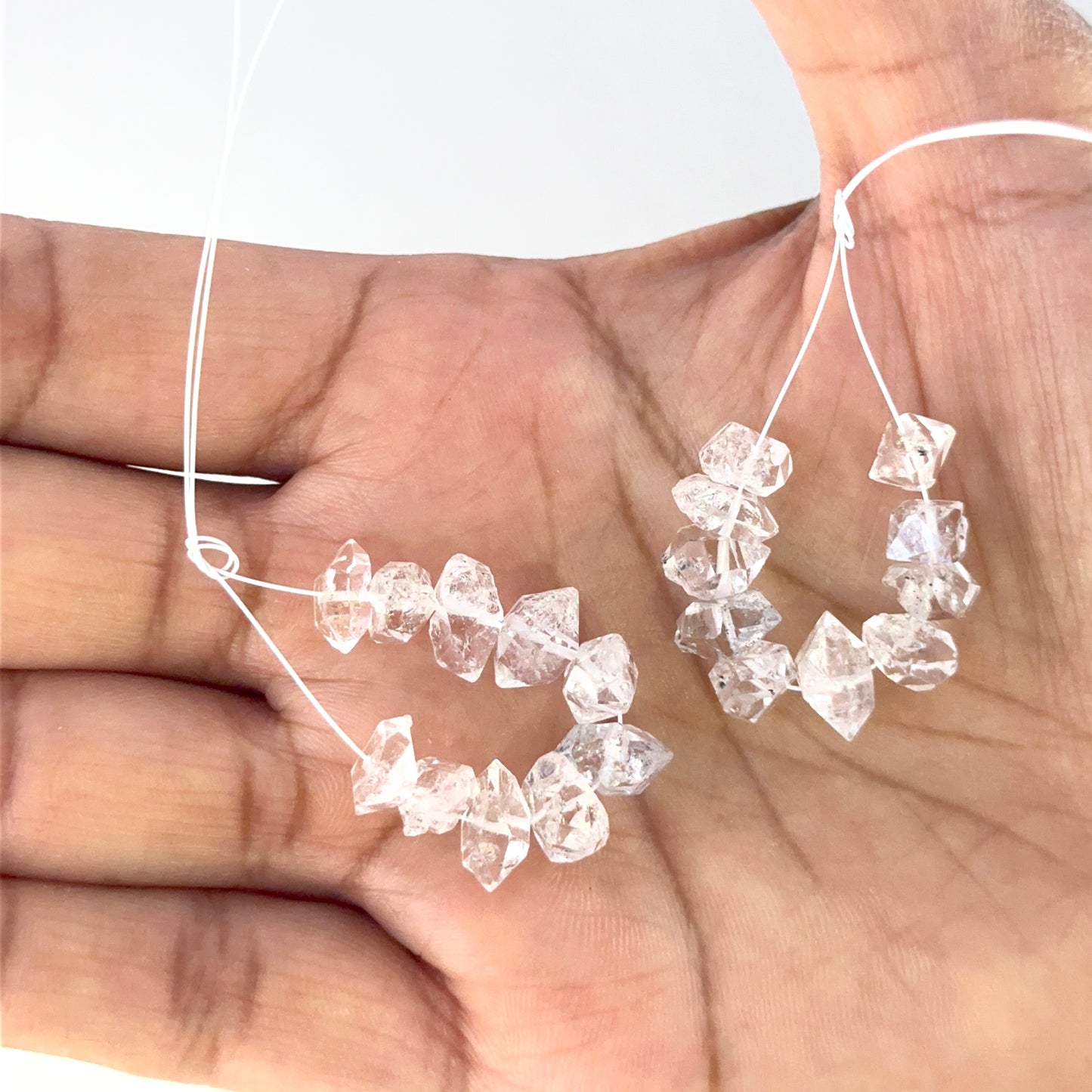 A person holds rough drilled Herkimer Diamond crystals, highlighting their clarity.

