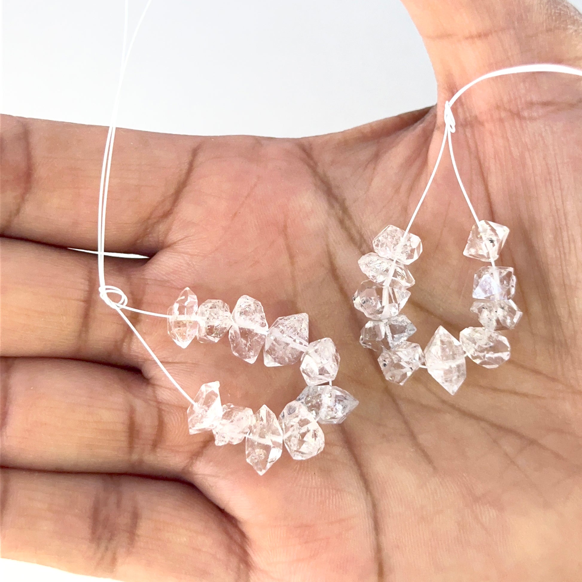 A person holds rough drilled Herkimer Diamond crystals, highlighting their clarity.

