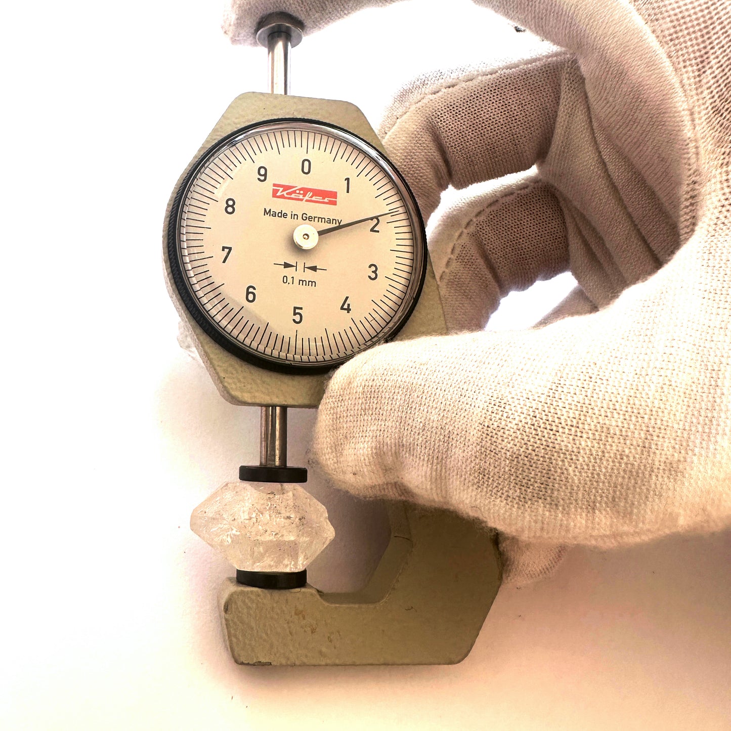 A dial gauge measures the Herkimer rough nugget 10-15mm gemstone for precision.