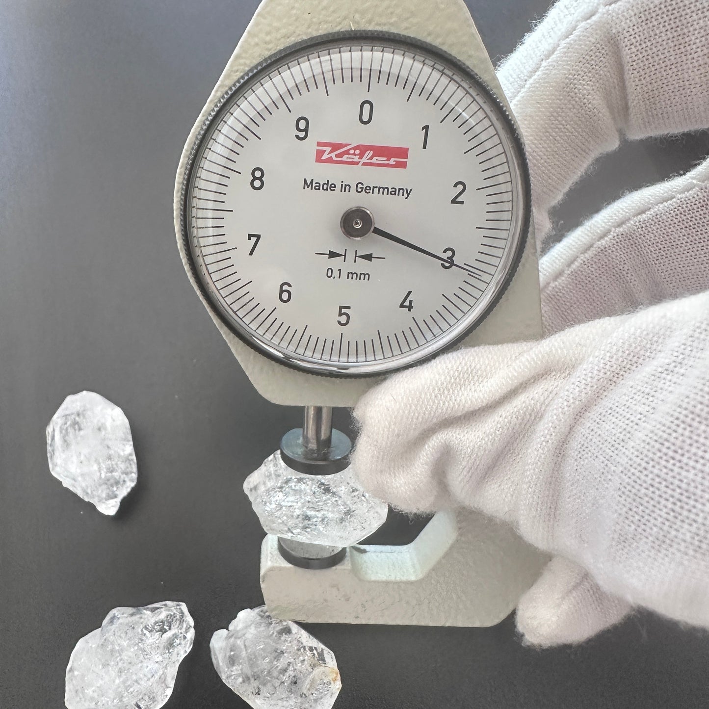 A dial gauge measures the Herkimer Diamond rough cut 13-14mm gemstone.