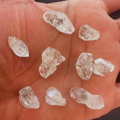 A person holds delicate strands of Herkimer diamond gemstone, showcasing their organic cut and shine.
