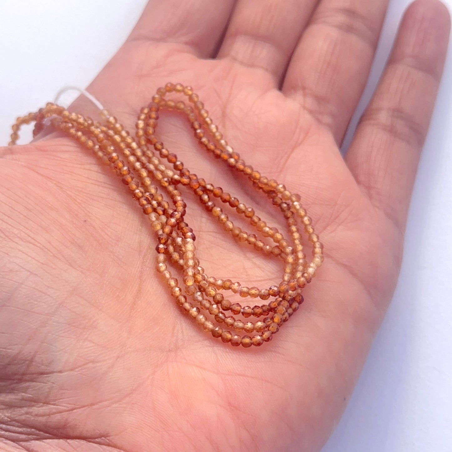 A person holds delicate strands of hessonite beads, showcasing their smooth design.