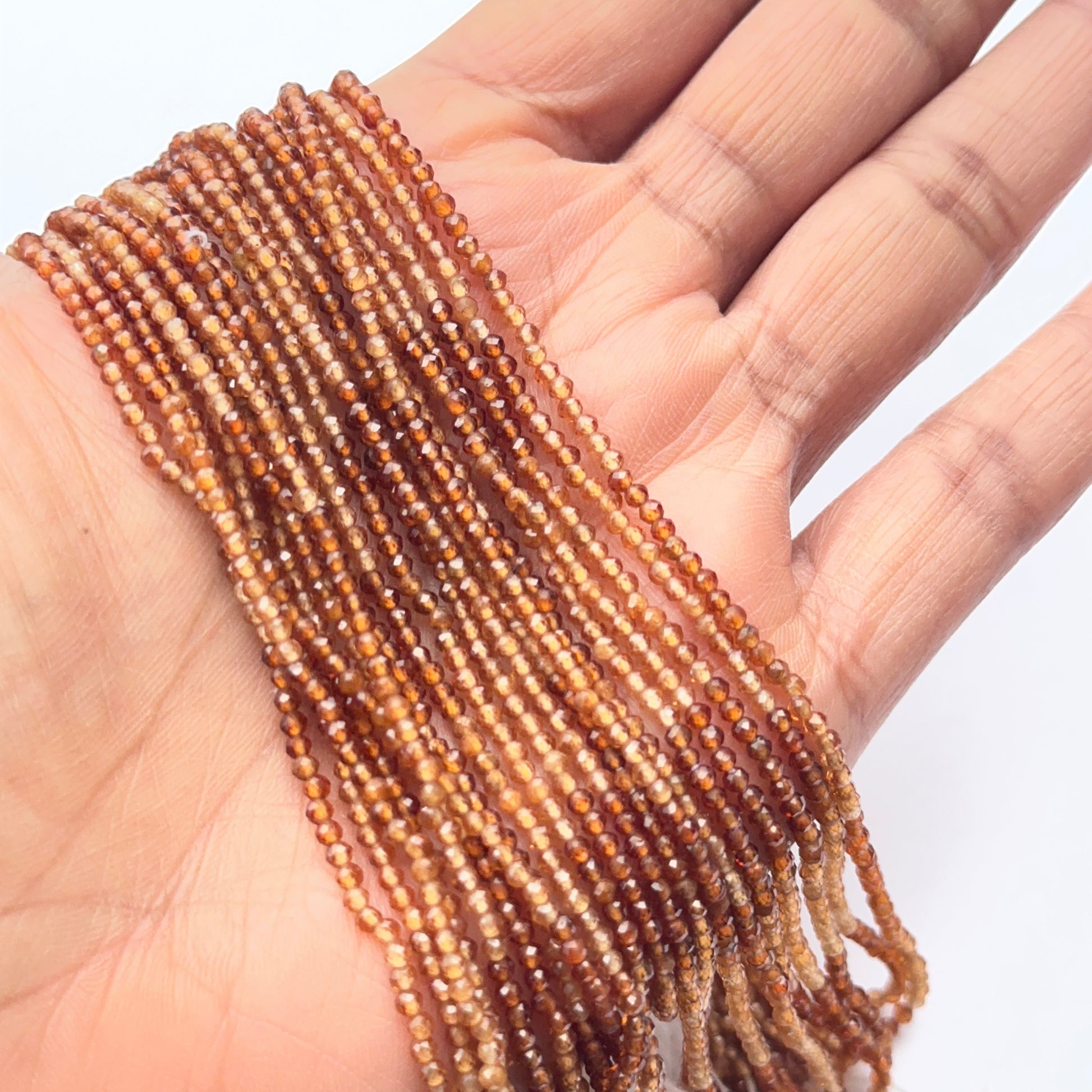 A person holds delicate strands of hessonite beads, showcasing their smooth design.