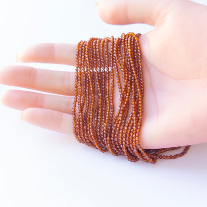 A person holds delicate strands of Hessonite beads, showcasing their faceted rondelle design.