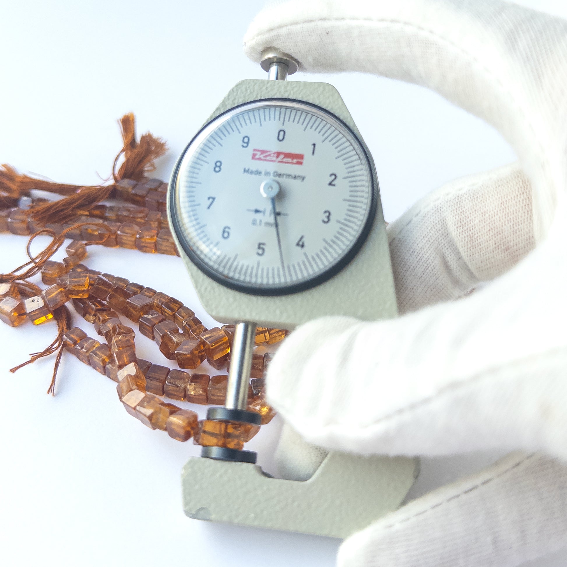 A dial gauge measures the Hessonite smooth cube 5mm gemstone.