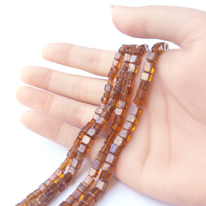 A person holds delicate strands of Hessonite beads, showcasing their smooth cube design.