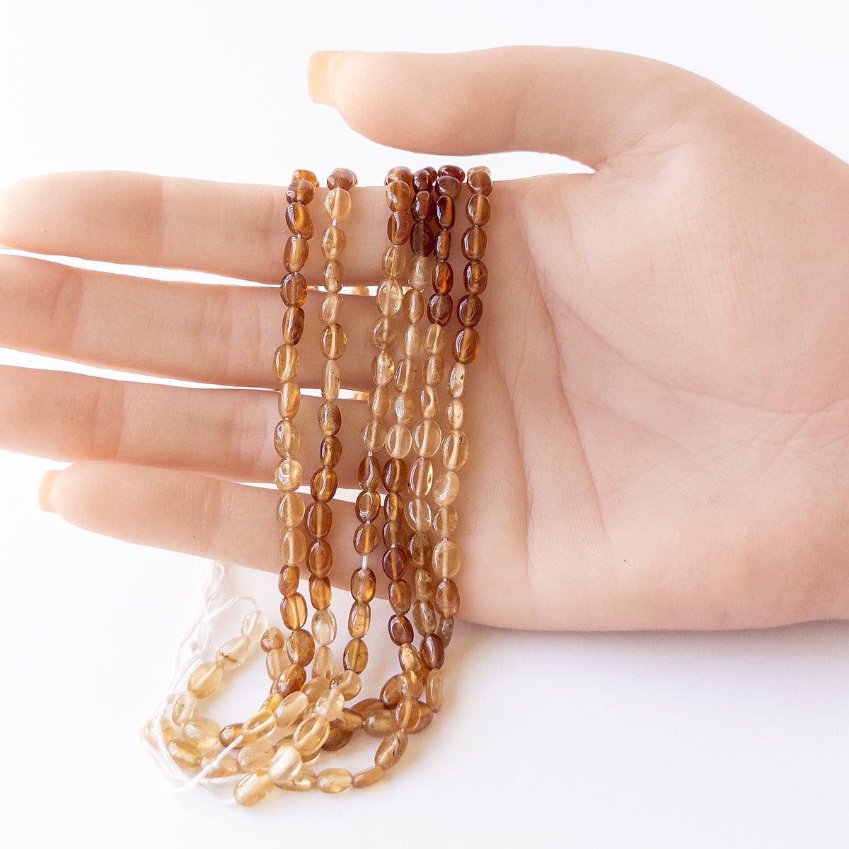 A person holds delicate strands of Hessonite beads, showcasing their smooth oval design.