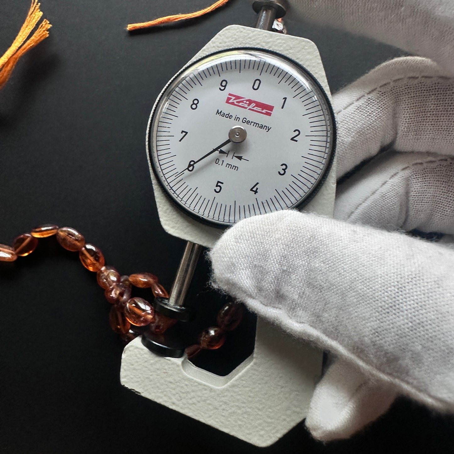 A dial gauge measures the Hessonite oval 7.5–9x6mm gemstone.