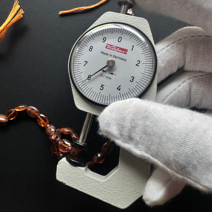 A dial gauge measures the Hessonite oval 7.5–9x6mm gemstone.