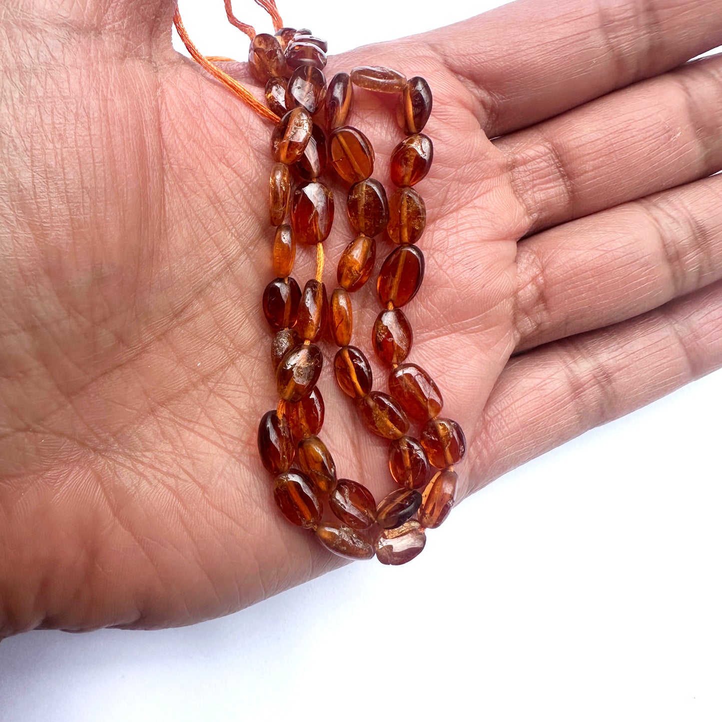 A person holds delicate strands of Hessonite beads, showcasing their smooth design. 