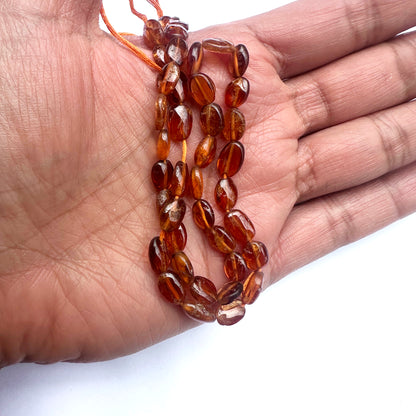 A person holds delicate strands of Hessonite beads, showcasing their smooth design. 
