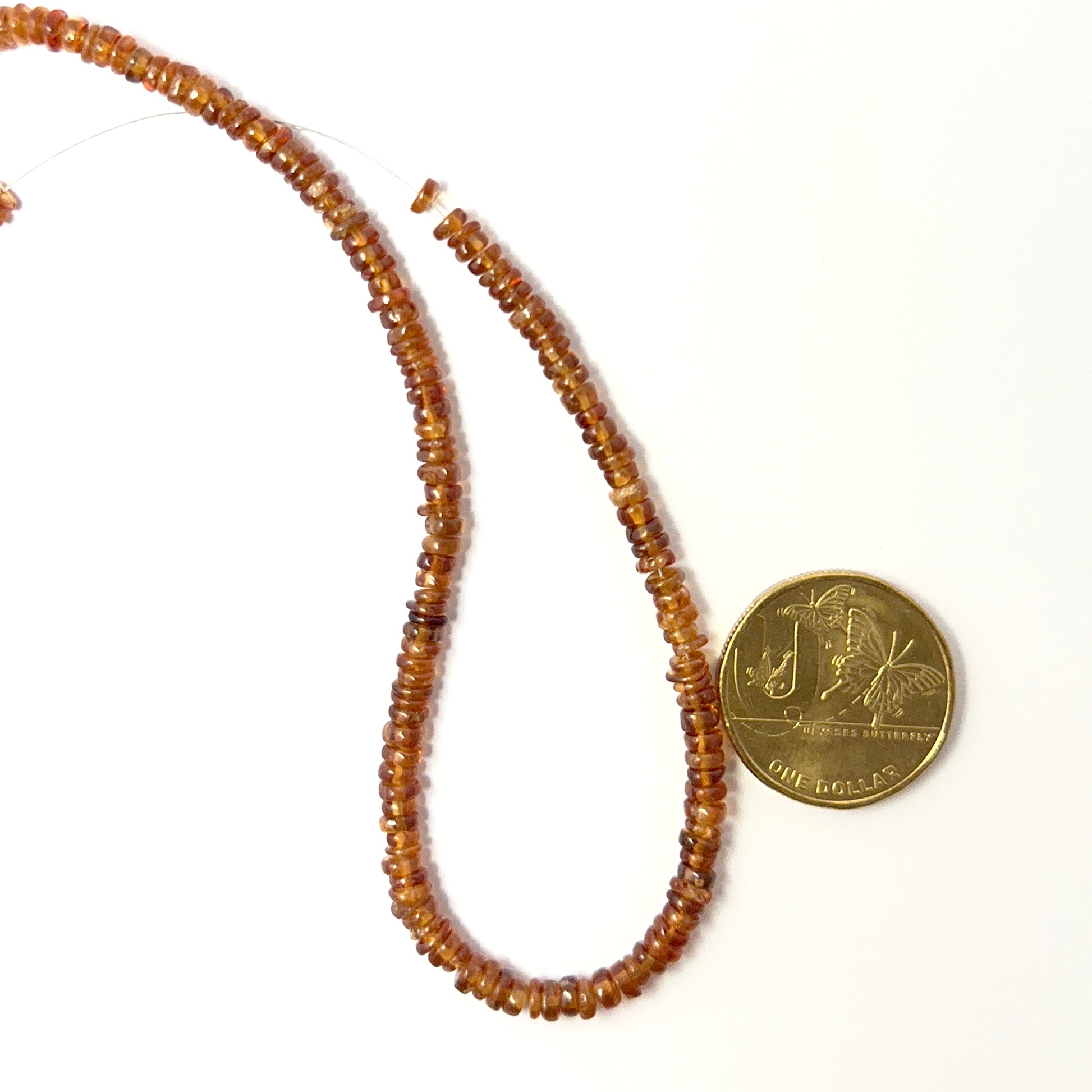 A coin is place near delicate strands of Hessonite beads for scale.