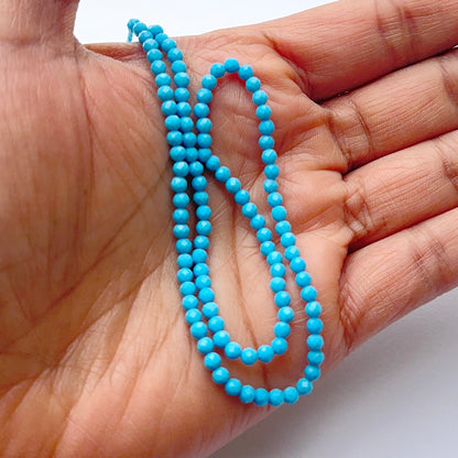 A person holds delicate strands of howlite turquoise faceted beads, showcasing their smooth design.