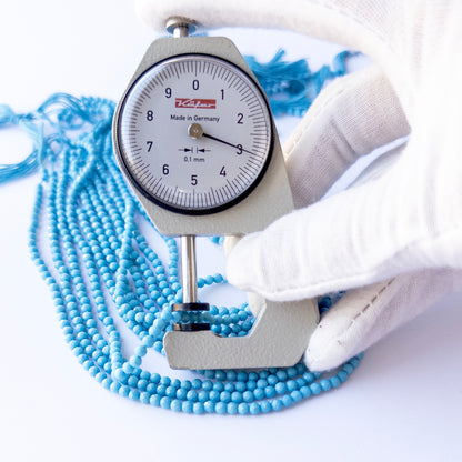 A dial gauge measures the Howlite Turquoise faceted rondelle 3.1mm gemstone bead.