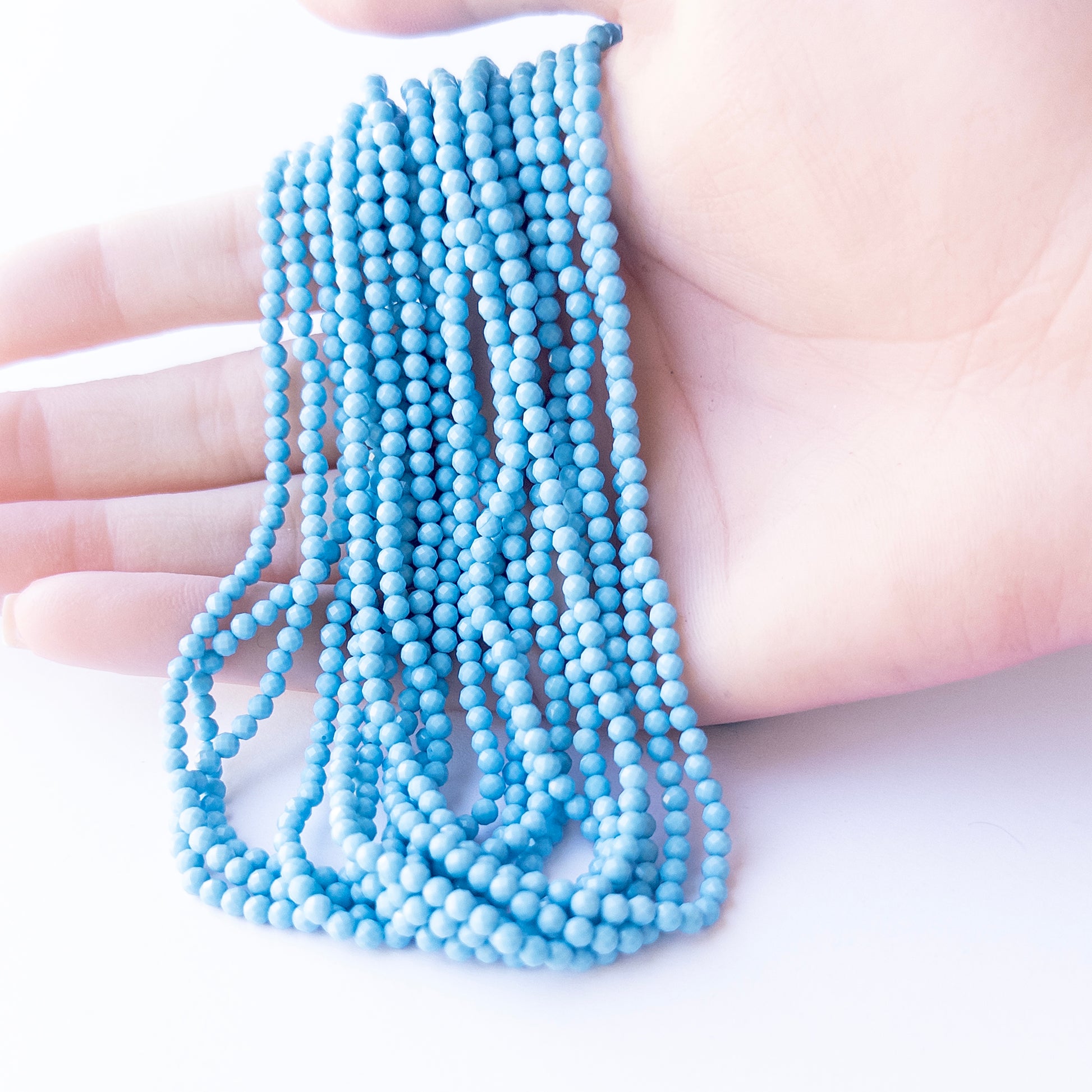 A person holds delicate strands of Howlite Turquoise beads, showcasing their faceted rondelle design.