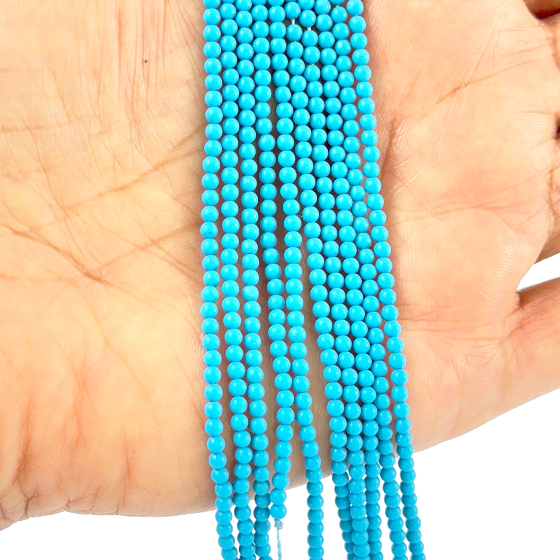 A person holds delicate strands of Howlite Turquoise beads, showcasing their smooth design.