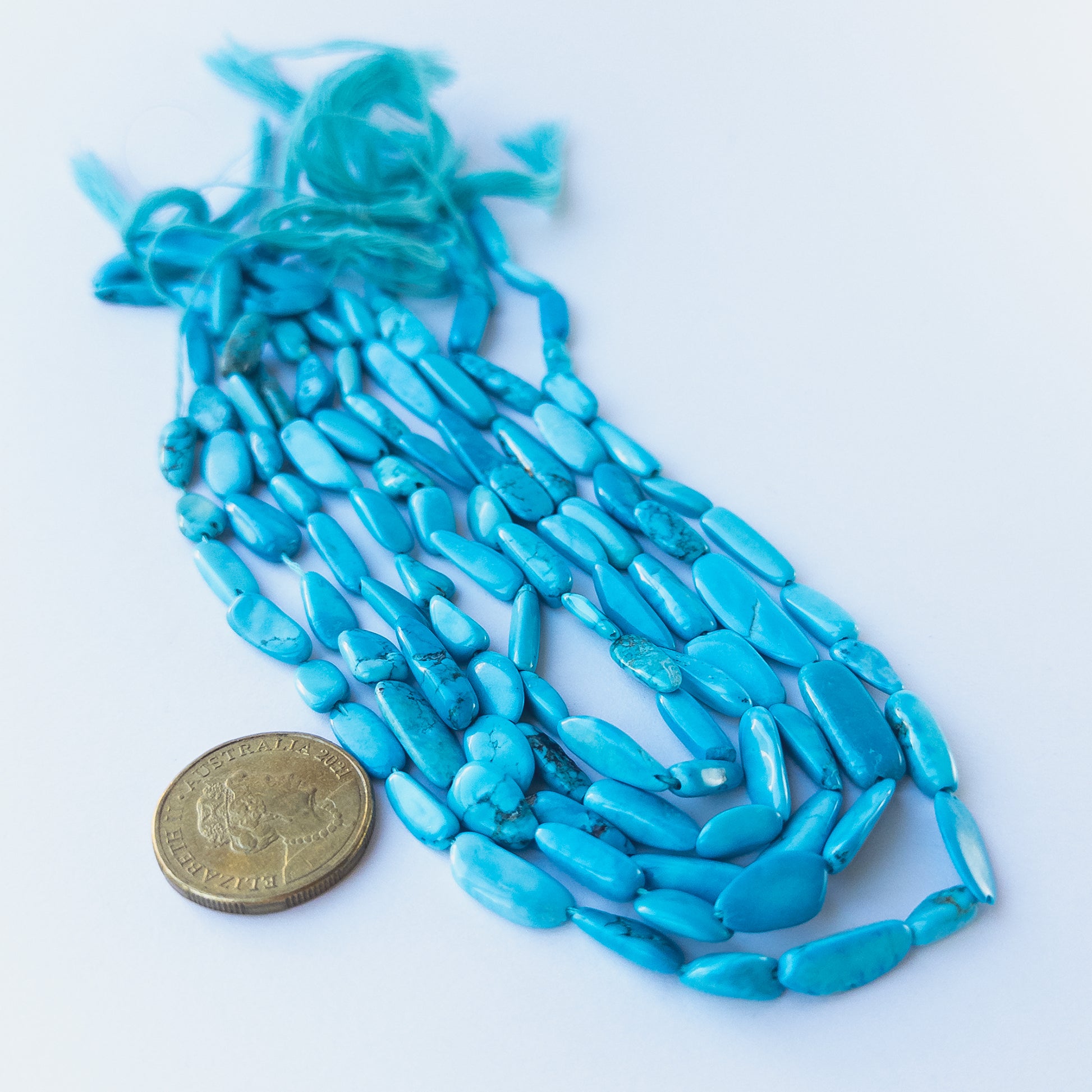 A coin is place near delicate strands of Howlite Turquoise beads for scale.