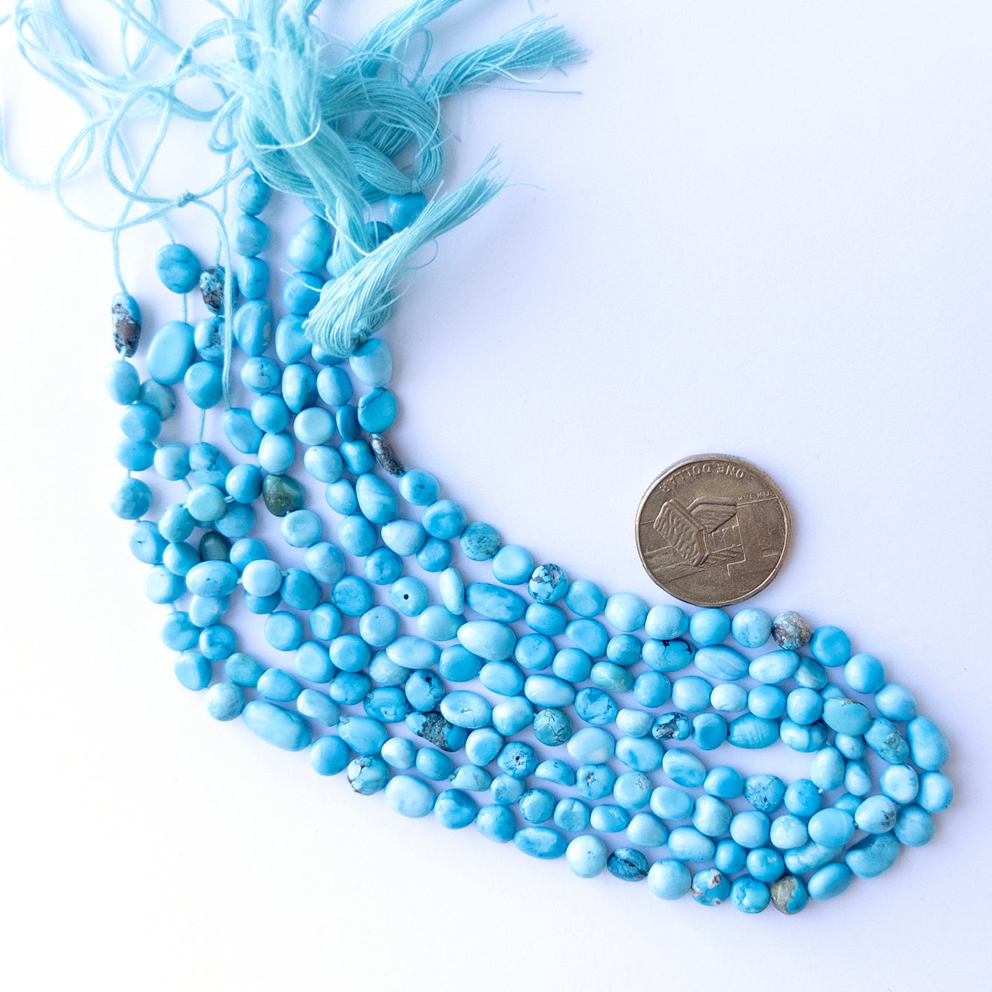 A coin is placed near delicate strands of Howlite Turquoise beads for scale.