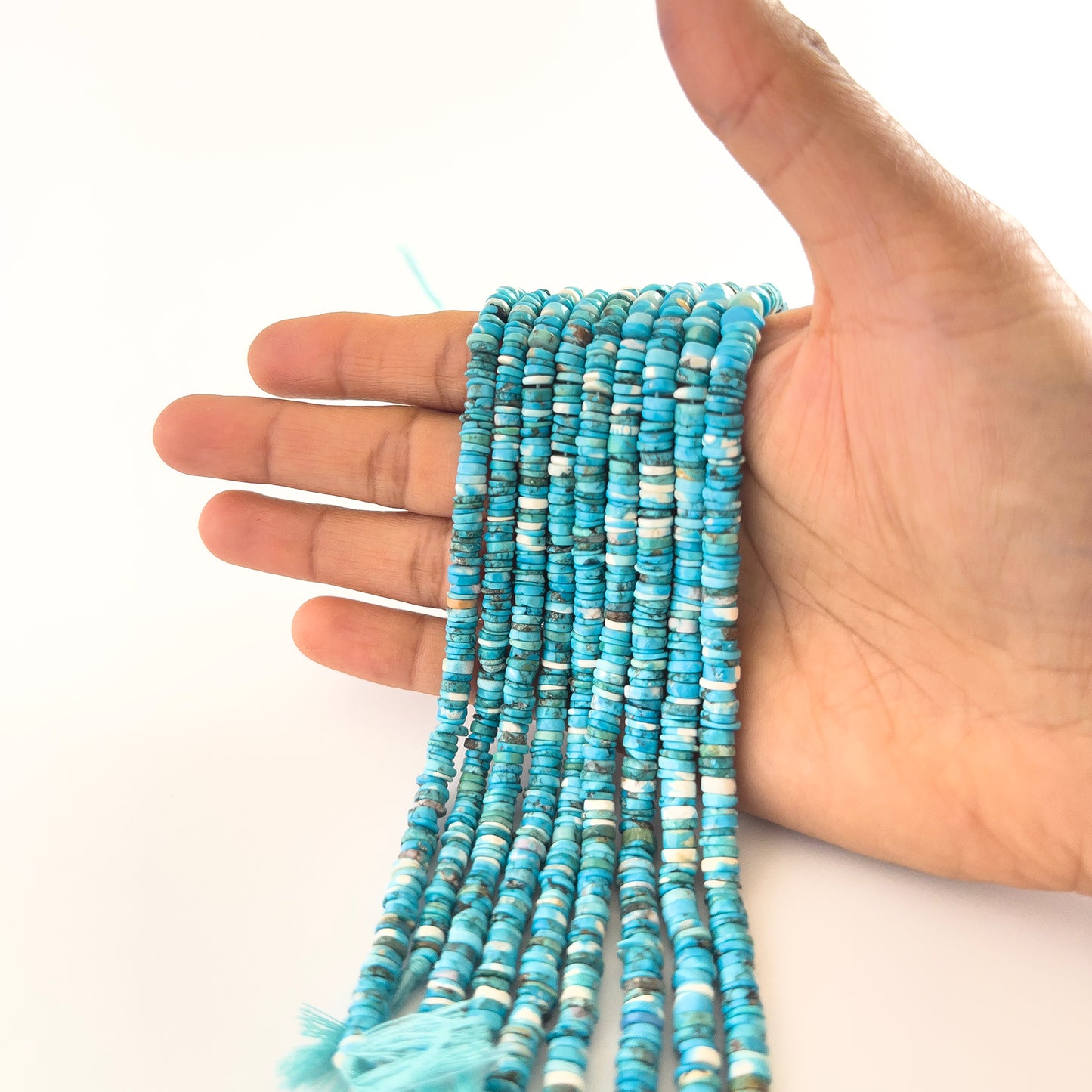 A person holds Howlite Turquoise smooth wheel beads, showing their rounded heishi design and vivid colour.