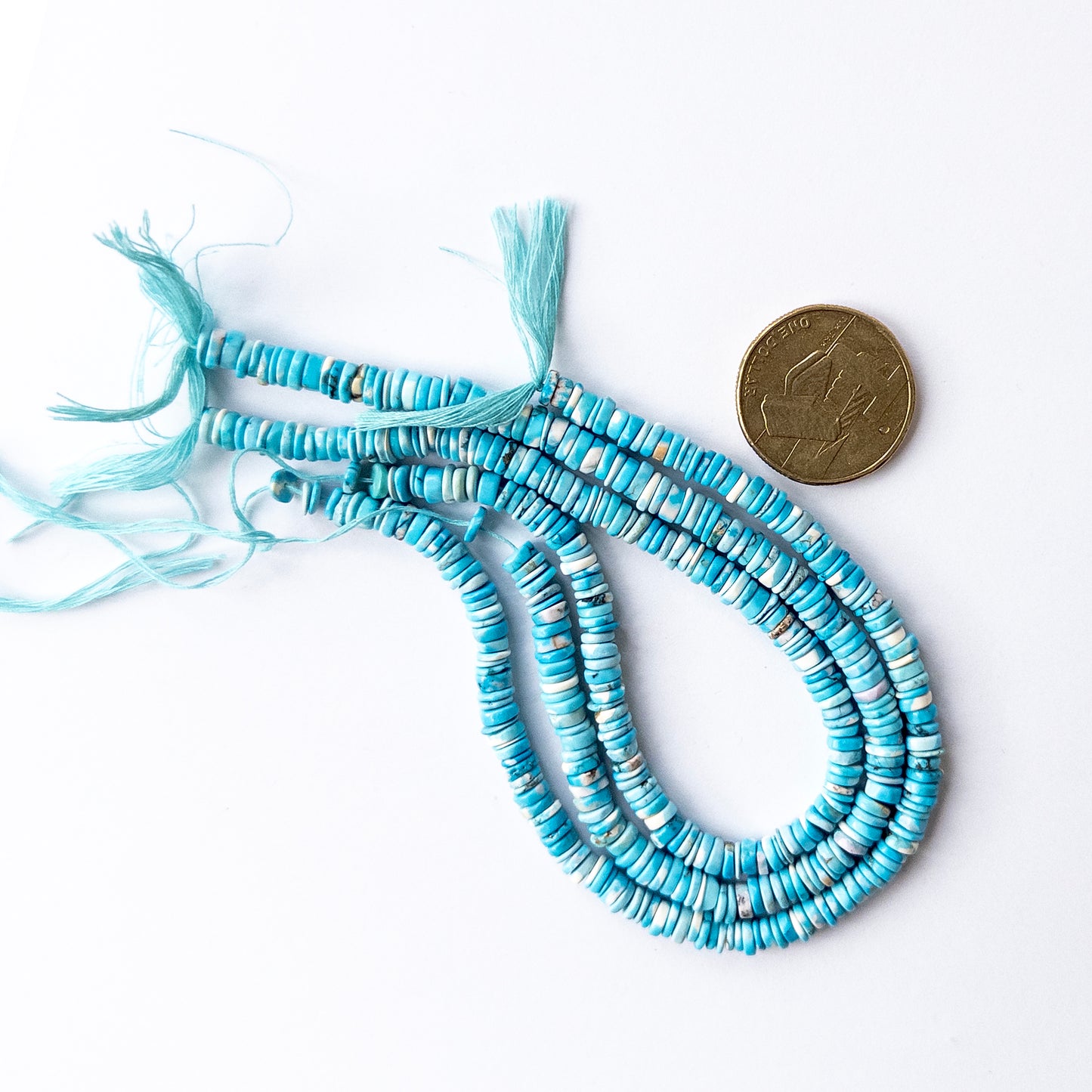 A coin is place near delicate strands of Howlite Turquoise beads for scale.

